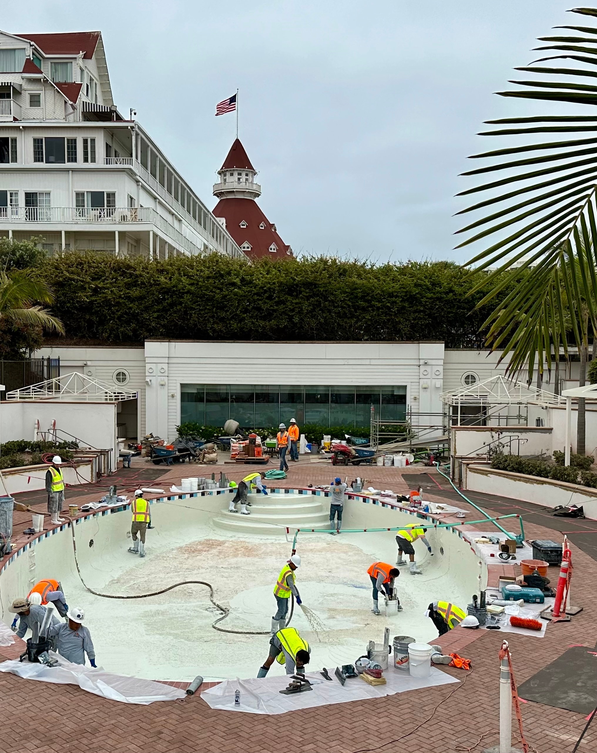 Sol Pacific Pool Plastering crew resurfacing a pool at Hotel del Coronado in San Diego, with the historic red-turret resort visible in the background